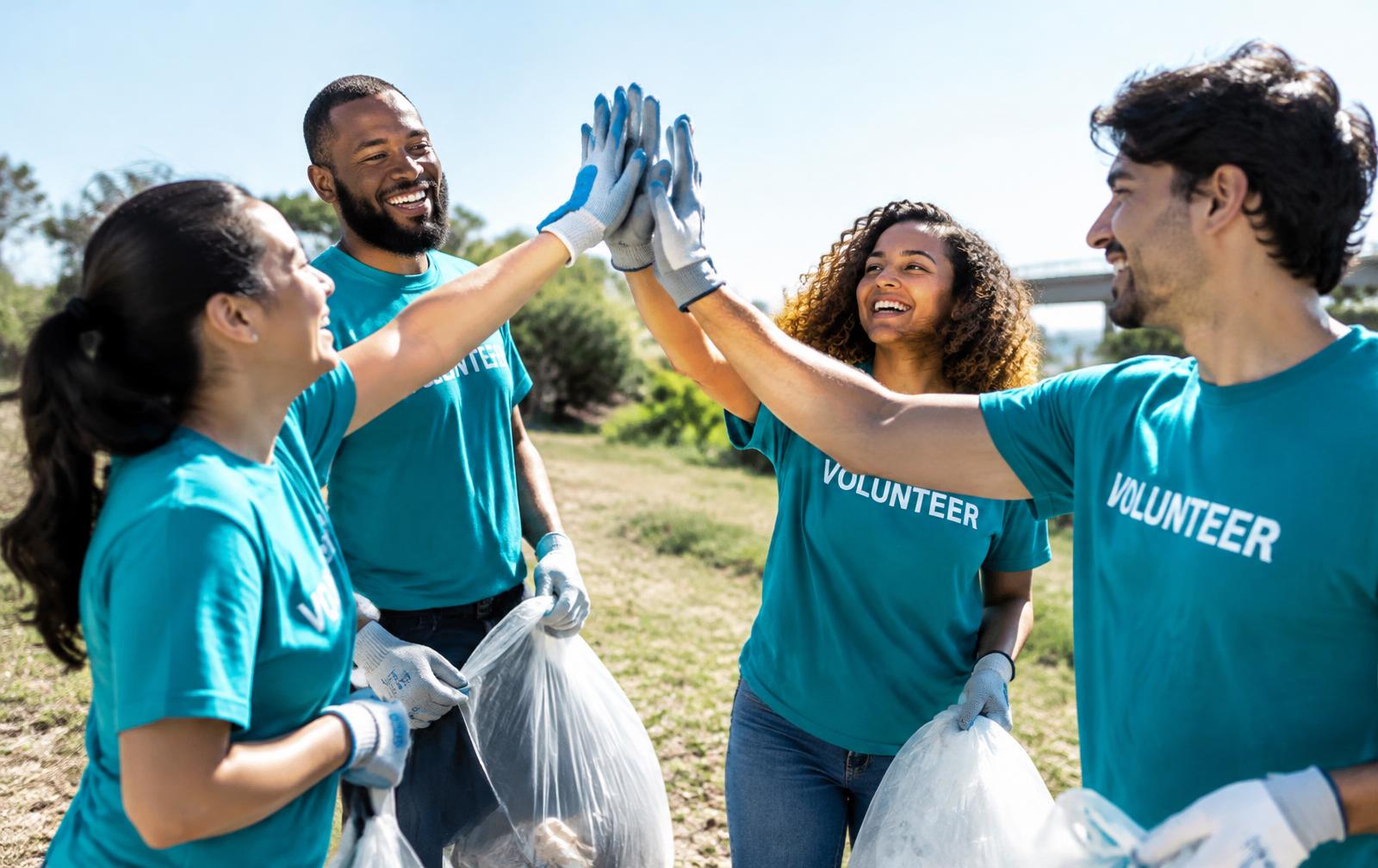 Volunteers in teal shirts giving each other a high-five outdoors